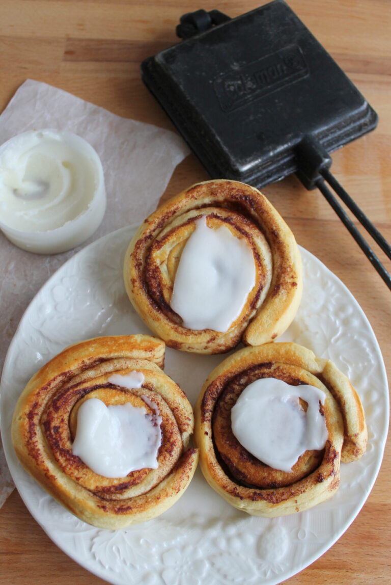 cinnamon buns on white plate with frosting with pie iron beside them